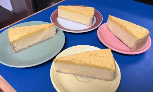 Four slices of cheesecake on colorful plates, arranged on a blue surface.