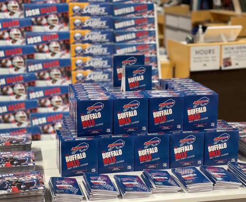 A display of Buffalo Bills calendars stacked on a table, with a backdrop of more calendars featuring Josh Allen.