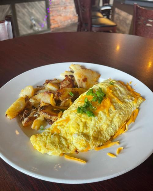 A fluffy cheese omelette topped with green onions, served with crispy golden-brown potato cubes on a white plate.