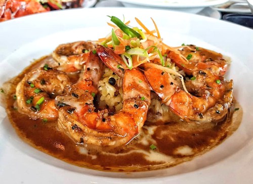 A plate of shrimp in a savory sauce, garnished with green onions and carrots, served over rice.