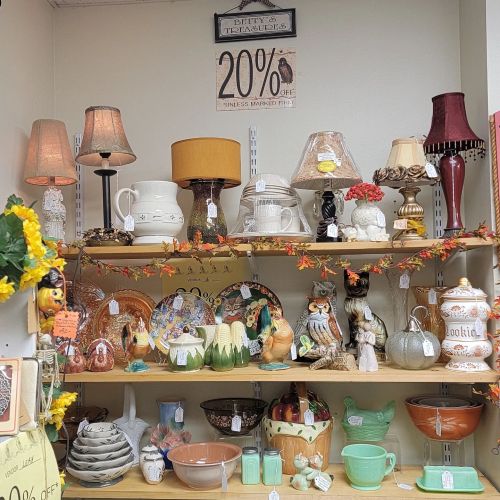 A display of various decorative items, including lamps, pottery, and figurines, on wooden shelves with autumn decor.