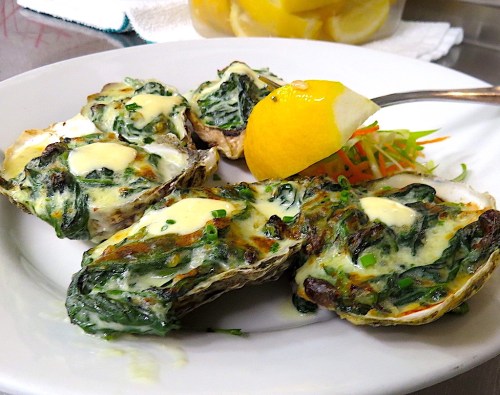 Baked oysters topped with creamy spinach and a lemon wedge on a white plate.