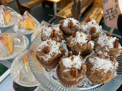 A glass platter of small desserts topped with coconut and pecans, with other cakes in the background.