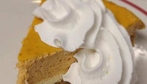 A slice of pumpkin pie topped with a generous swirl of whipped cream on a white plate.