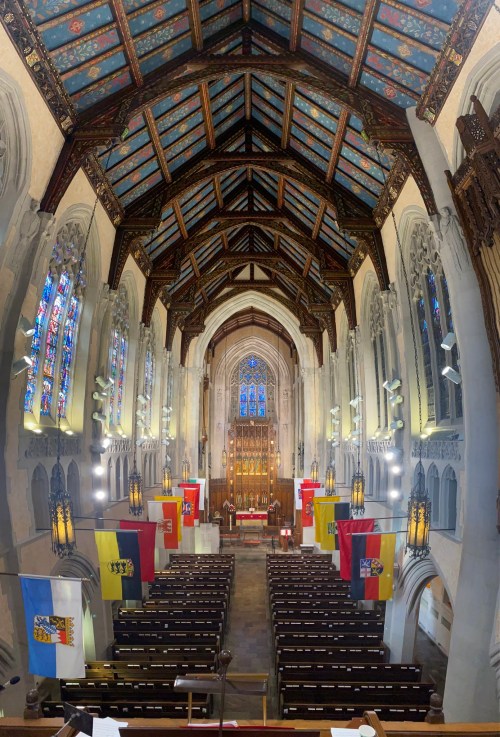 Interior of a grand church with stained glass windows, wooden beams, and colorful banners hanging from the walls.