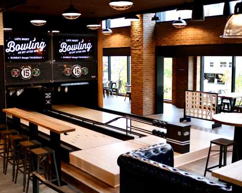 Interior of a modern bowling alley with lanes, seating, and large screens displaying "Late Night Bowling" promotions.