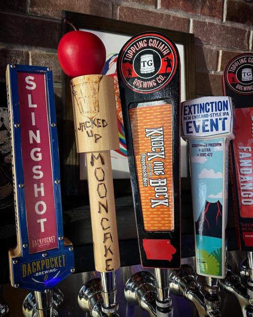 A collection of colorful beer taps featuring unique designs and names like "Slingshot" and "Jacked Up Mooncake."