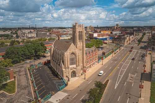 Aerial view of a historic church on a city street, surrounded by buildings and under a partly cloudy sky.