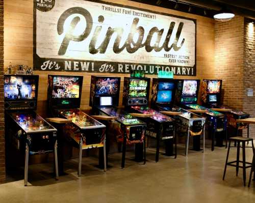 A row of colorful pinball machines against a brick wall with a vintage "Pinball" sign above.