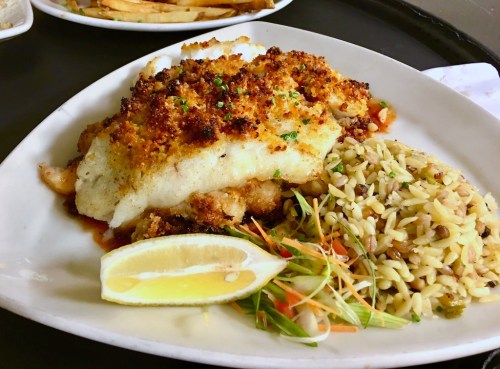 A plate of baked fish with a crispy topping, served with orzo rice and a lemon wedge, garnished with vegetables.