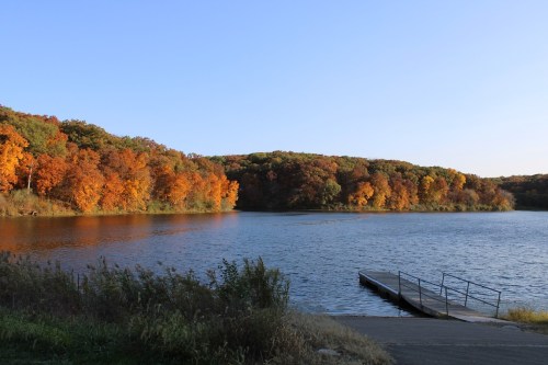 A serene lake surrounded by vibrant autumn foliage and a small dock extending into the water.