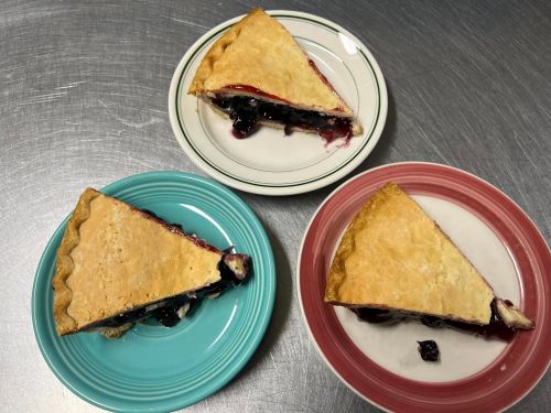 Three slices of berry pie on colorful plates, showcasing flaky crust and rich filling.