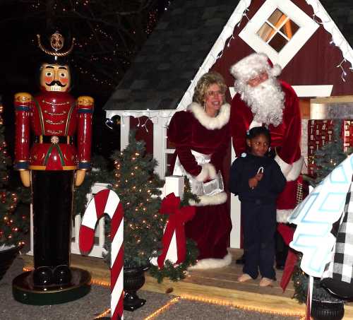 A festive scene with Santa, Mrs. Claus, and a child in front of a decorated house, featuring a nutcracker and candy canes.