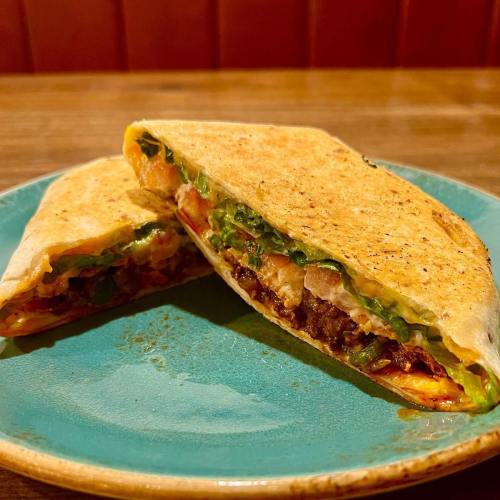 A cut quesadilla on a blue plate, filled with vegetables and melted cheese, showcasing a golden-brown tortilla.