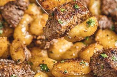 A close-up of tender beef chunks and golden gnocchi, garnished with herbs and sprinkled with cheese.