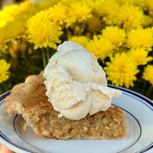 A slice of pie topped with vanilla ice cream, set against a backdrop of bright yellow flowers.