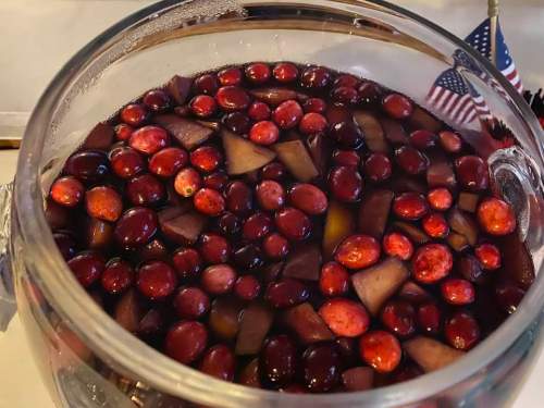A glass bowl filled with cranberry juice, cranberries, and diced apples, with a small American flag in the background.