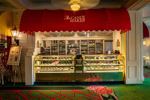 A candy shop display with glass cases filled with sweets, under a red awning that reads "The Candy Maker."