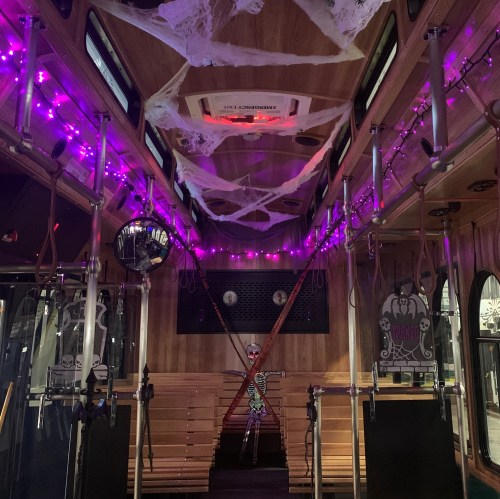 A decorated tram interior with purple lights, cobwebs, and a skeleton figure, creating a spooky atmosphere.