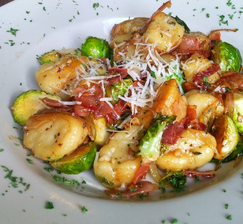 A plate of gnocchi with Brussels sprouts, crispy bacon, and grated cheese, garnished with parsley.