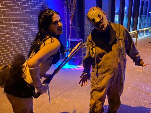 A woman in a costume poses with a man in a creepy mask, both in a dimly lit outdoor setting.