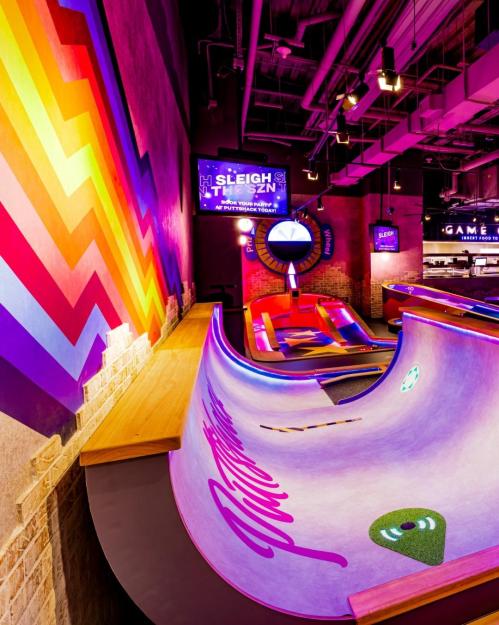 Colorful indoor mini-golf course with a curved ramp and vibrant wall art in a lively entertainment space.