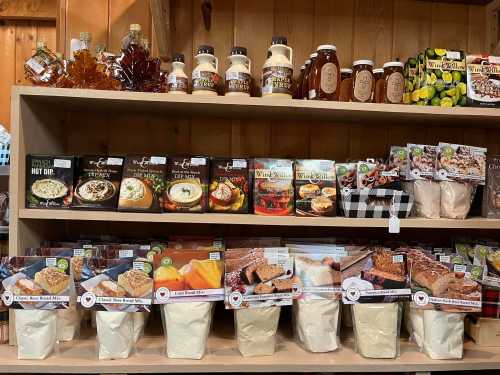 A wooden shelf displaying various packaged food items, including mixes, syrups, and jars of honey.