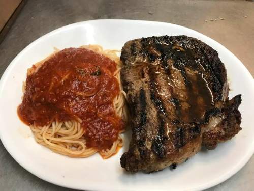 A plate featuring grilled steak alongside spaghetti topped with marinara sauce.