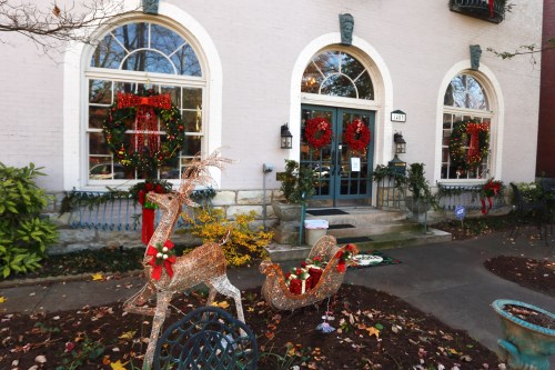 A festive building entrance decorated with wreaths and holiday lights, featuring a reindeer and sleigh in the foreground.