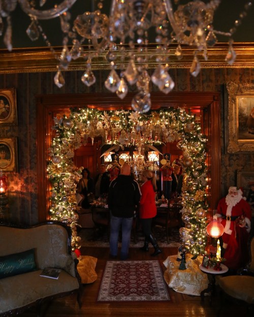 A festive room decorated for Christmas, featuring an arch of greenery and lights, with people and a Santa figure nearby.