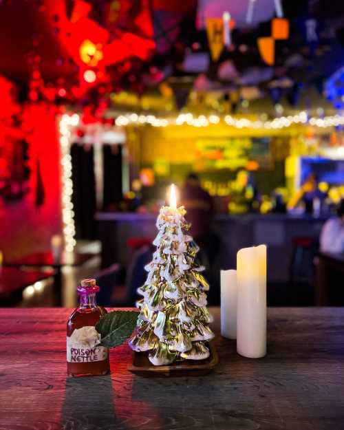 A festive scene featuring a decorative tree, a candle, and a bottle labeled "Poison" on a bar table with colorful lights.