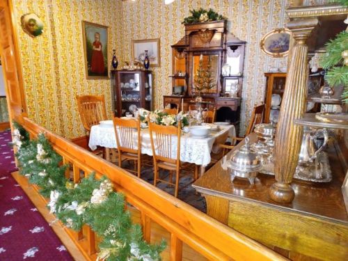 A vintage dining room with a decorated table, wooden furniture, and floral wallpaper, adorned with holiday greenery.