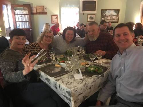 A group of five people smiling around a dining table set with plates and glasses in a cozy restaurant setting.