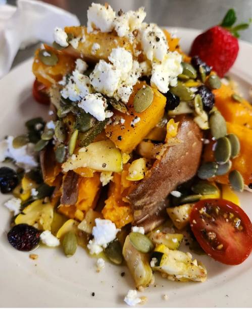 A plate of sweet potatoes topped with feta cheese, pumpkin seeds, cherry tomatoes, and mixed fruits.