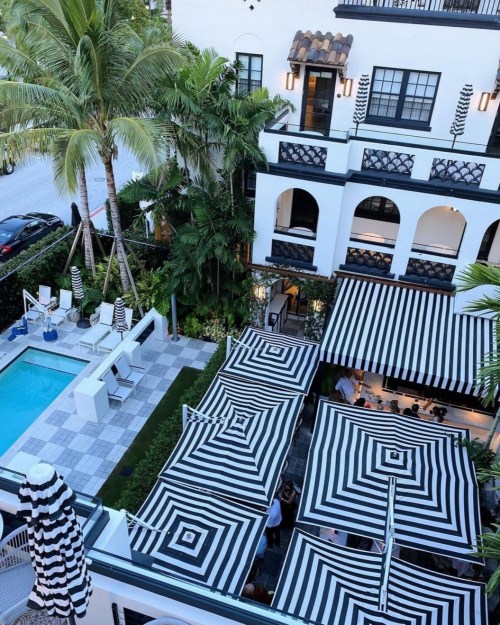 Aerial view of a stylish hotel with a pool, striped umbrellas, and lush greenery.