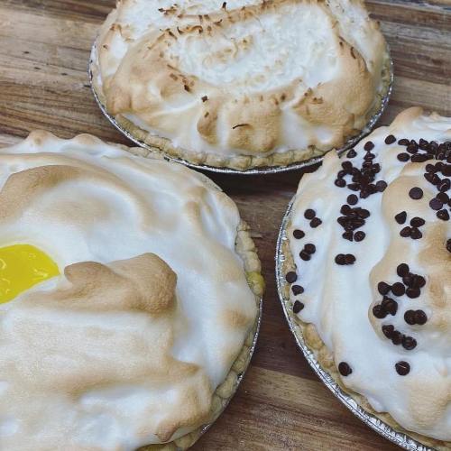 Three pies on a wooden surface: one with a yellow center, one topped with toasted meringue, and one with chocolate chips.