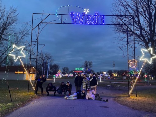 A group of people poses under a lit "Wish" archway at a festive outdoor light display.