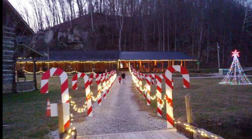 A festive pathway lined with candy cane decorations leads to a warmly lit building and a Christmas tree in the background.