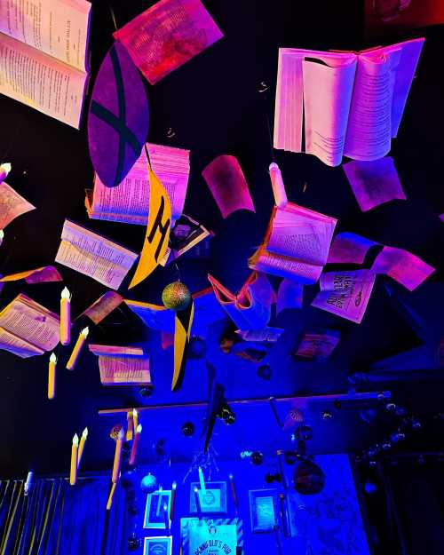 A ceiling adorned with floating books, candles, and colorful decorations, illuminated by blue and purple lights.