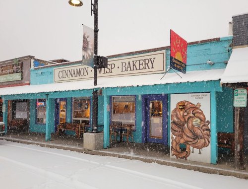 A colorful bakery storefront with a large sign, snowy street, and decorative window displays.