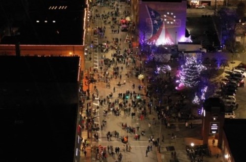 Aerial view of a bustling street filled with people, festive lights, and decorations during a nighttime event.