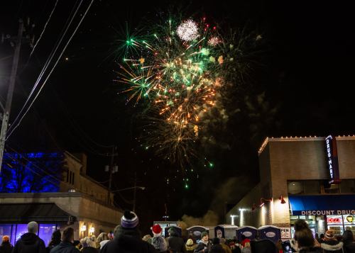 Crowd watching colorful fireworks display in the night sky over a city street.