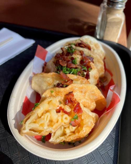 A close-up of three golden, crispy pastries filled with macaroni and cheese, topped with bacon and herbs.