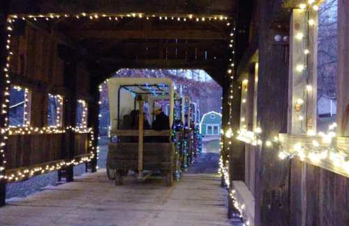 A covered bridge adorned with colorful lights, with a wagon passing through, creating a festive atmosphere.