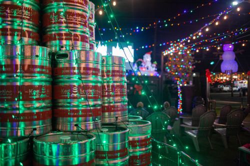 A stack of beer kegs illuminated by colorful holiday lights in a festive outdoor setting.