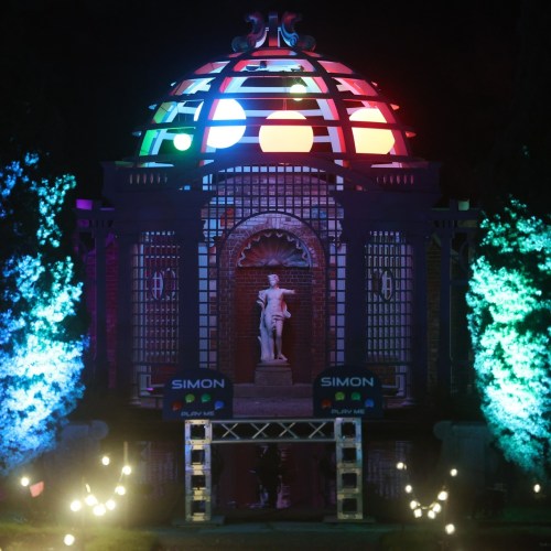 A brightly lit structure with a dome, featuring colorful lights and a statue, surrounded by illuminated trees at night.