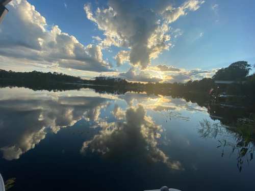 A serene lake at sunset, reflecting clouds and trees, with a vibrant sky and calm water.