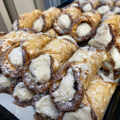 A close-up of freshly made cannoli, filled with creamy ricotta and dusted with powdered sugar.