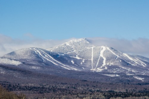 Snow-covered mountain peaks under a clear blue sky, with ski trails visible on the slopes.