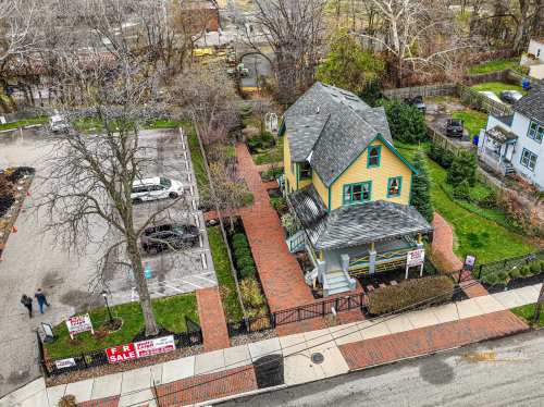 Aerial view of a colorful house for sale, surrounded by a landscaped yard and parking area.